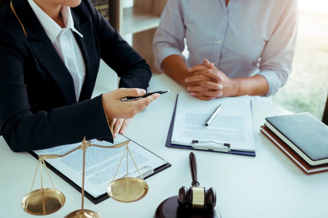 A lawyer talking to a client while holding a pen at a table with a gavel