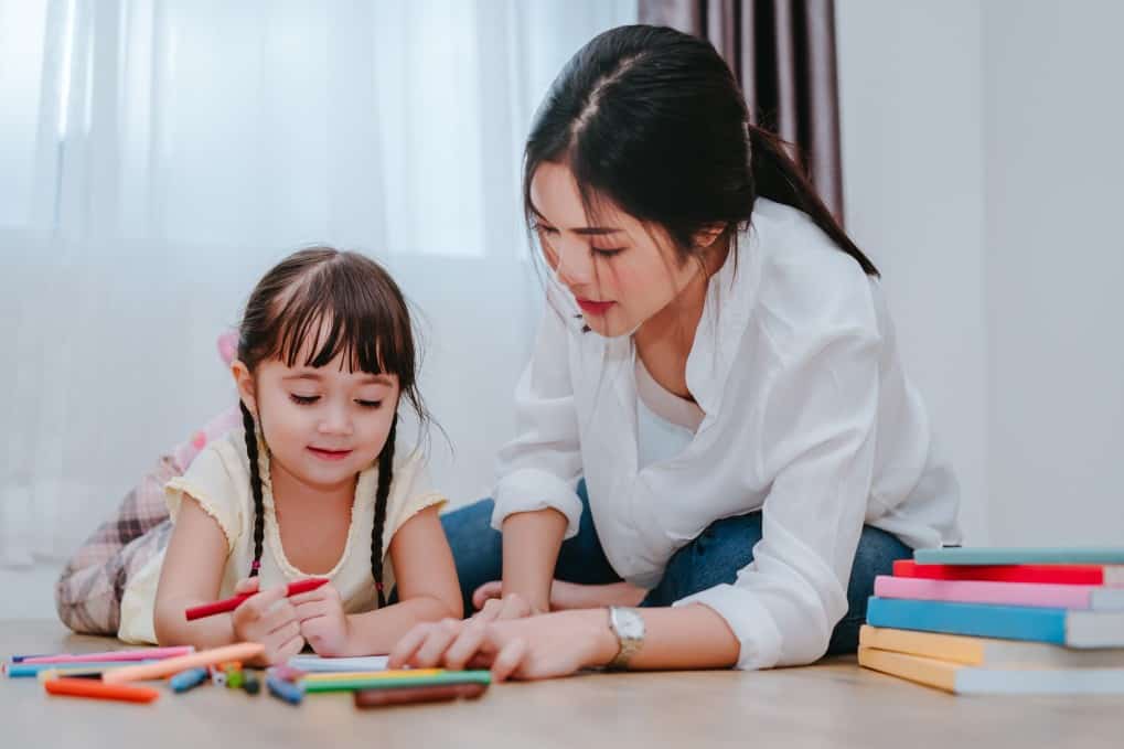 Mother sitting in the floor with her daughter while drawing with markers.